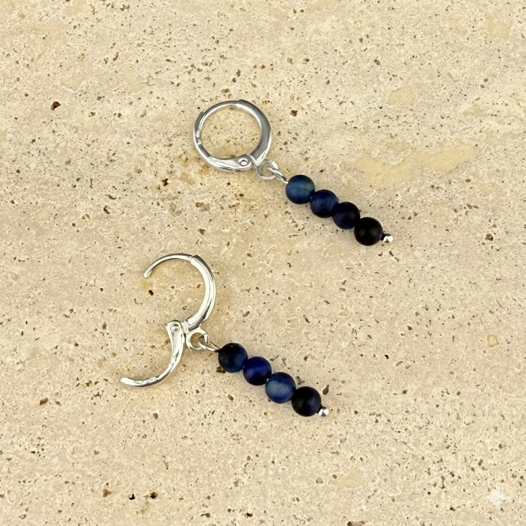 Silver variant of the Aking Sinta Blue Tiger Eye huggie earrings on marble; one silver hinge clasp is open, showing the four vertically stacked blue beads and a tiny silver seed bead at the base.