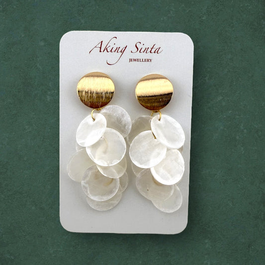 A pair of gold Cascading Capiz Shell Earrings with brushed finish studs mounted on a professional white cardboard display card; the "Aking Sinta" brand name is printed clearly at the top of the card against a dark green background