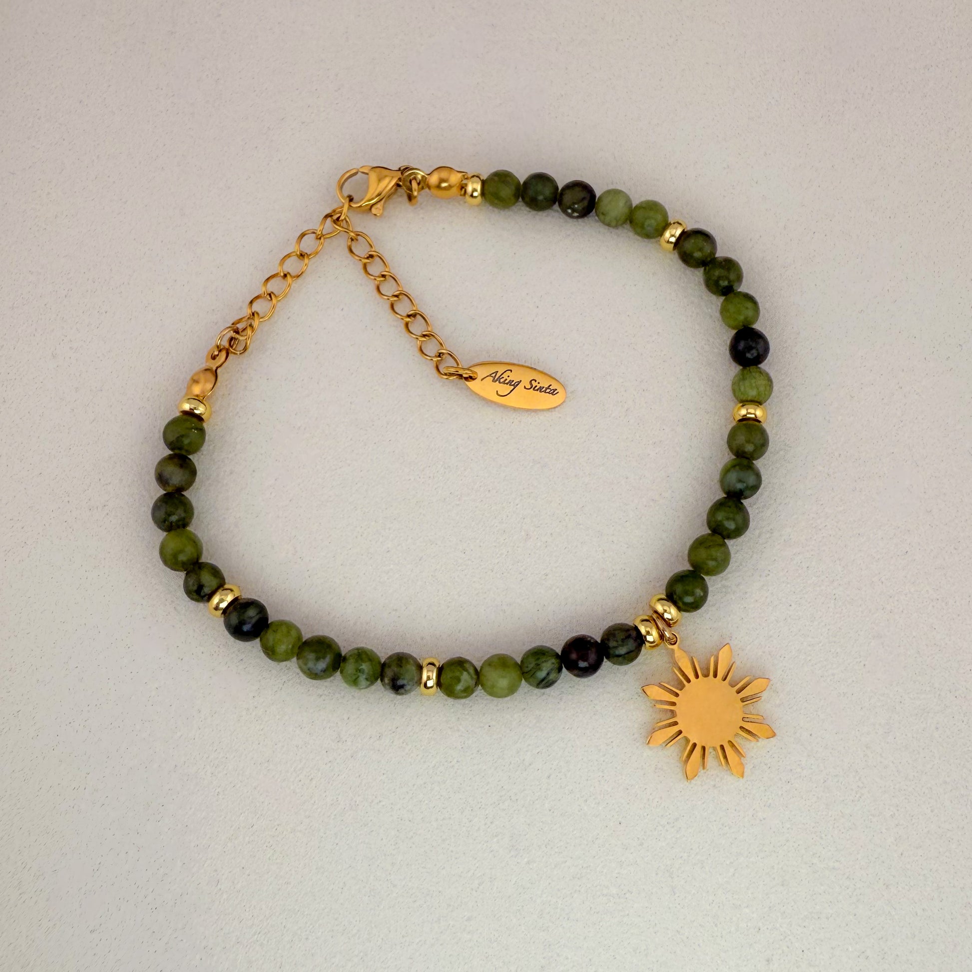 An Aking Sinta Canadian Jade beaded bracelet featuring smooth, translucent forest-green gemstones and a signature gold 8-ray Araw sun charm, displayed on a clean white background