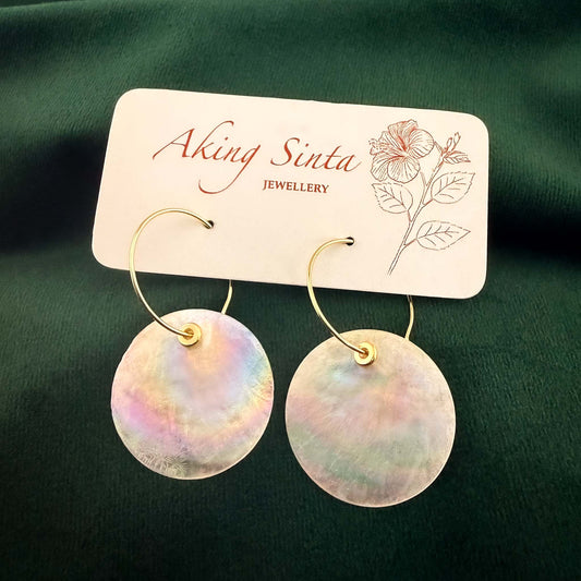 Capiz shell hoop earrings with metal bead accents on a white display card against a dark green background.