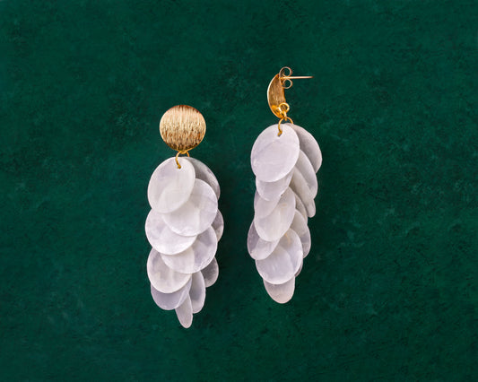 A pair of Aking Sinta gold cascading earrings on a dark green background; featuring a modern brushed-finish gold stud from which multiple iridescent white Capiz shell disks hang in a vertical, tiered sequence