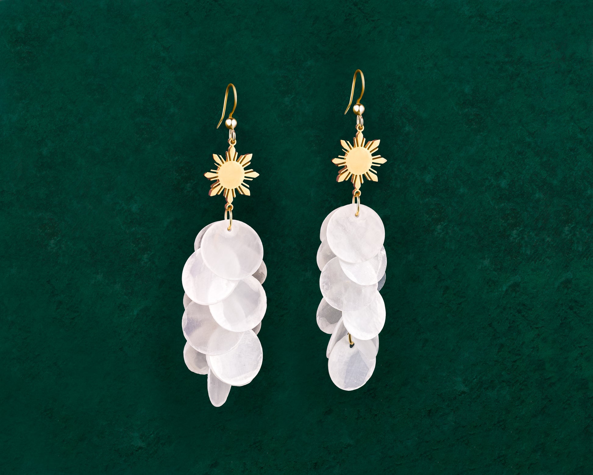 Aking Sinta Cascading Capiz Shell Hook Earrings with Araw sun charms displayed on dark green background, highlighting lightweight design and Philippine-inspired craftsmanship