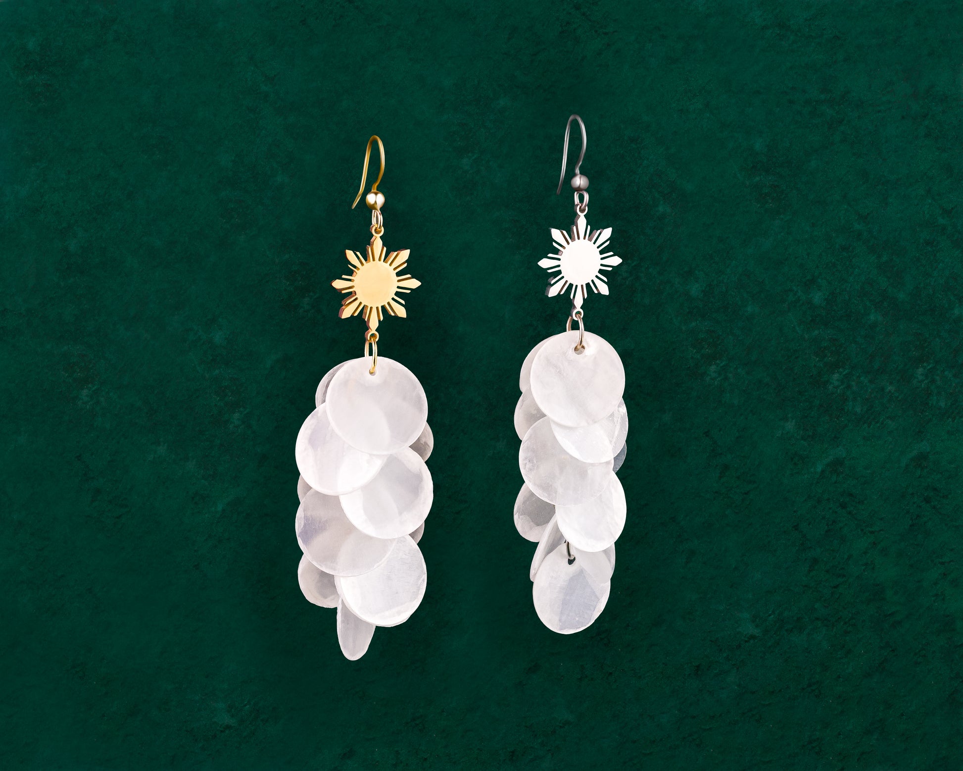Aking Sinta Cascading Capiz Shell Hook Earrings with Araw sun charms displayed on dark green background, highlighting lightweight design and Philippine-inspired craftsmanship