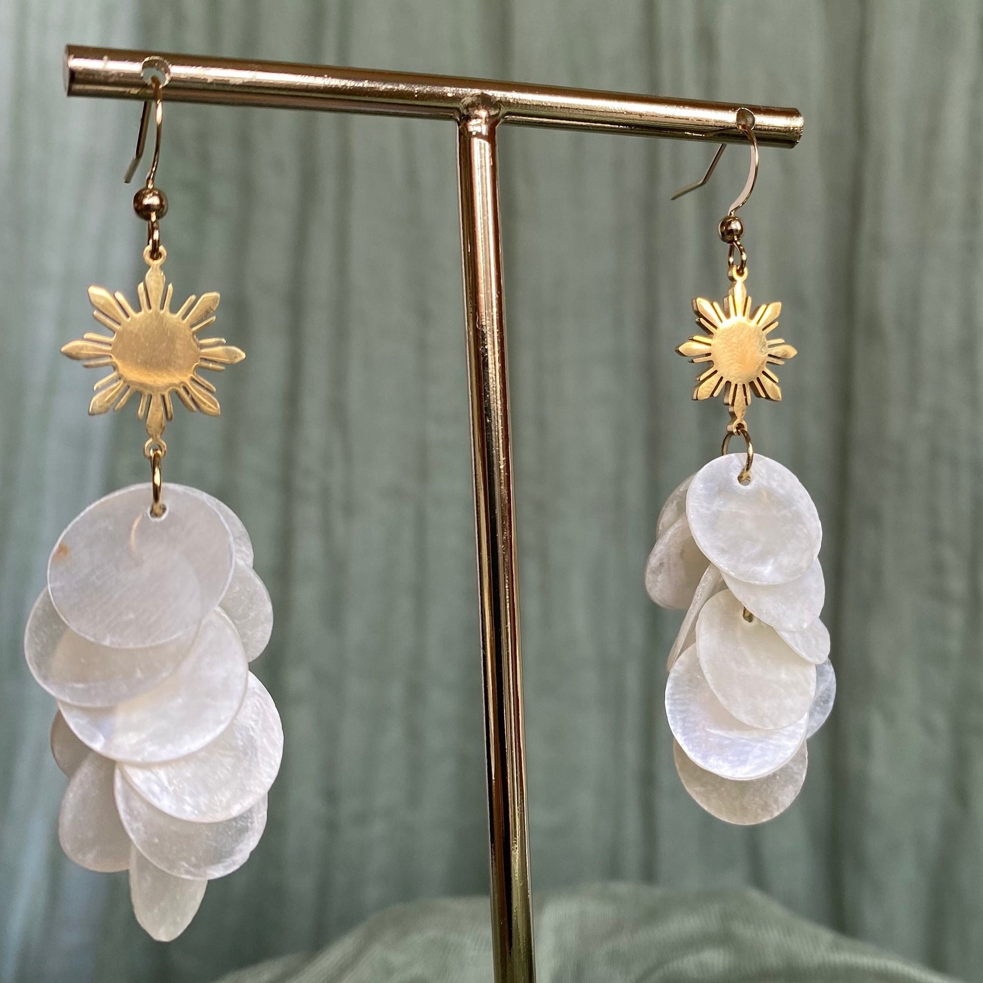 Aking Sinta Cascading Capiz Shell Hook Earrings with Araw sun charms displayed on metal holder with silver rod, one earring on each side, highlighting lightweight design and Philippine-inspired craftsmanship