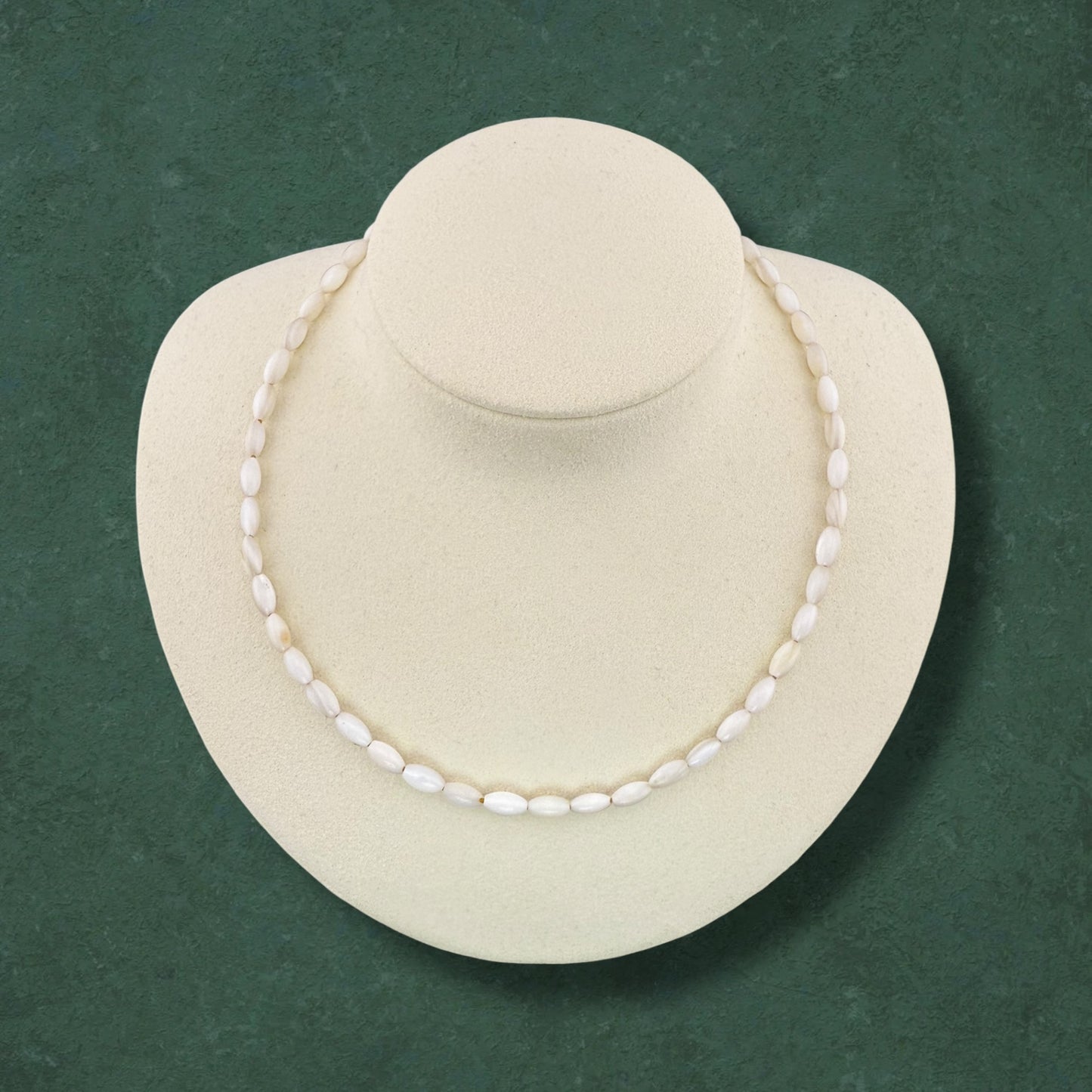 Aking Sinta necklace made entirely of white iridescent Mother of Pearl rice beads; a classic all-white strand displayed on a jewelry bust against a dark green background.