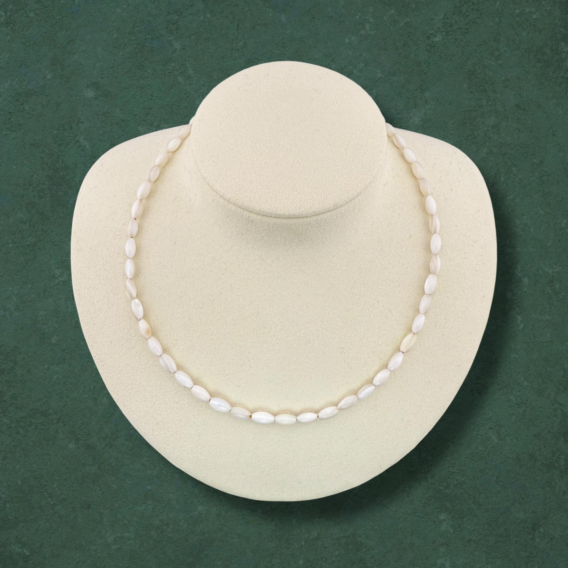 Aking Sinta necklace made entirely of white iridescent Mother of Pearl rice beads; a classic all-white strand displayed on a jewelry bust against a dark green background.
