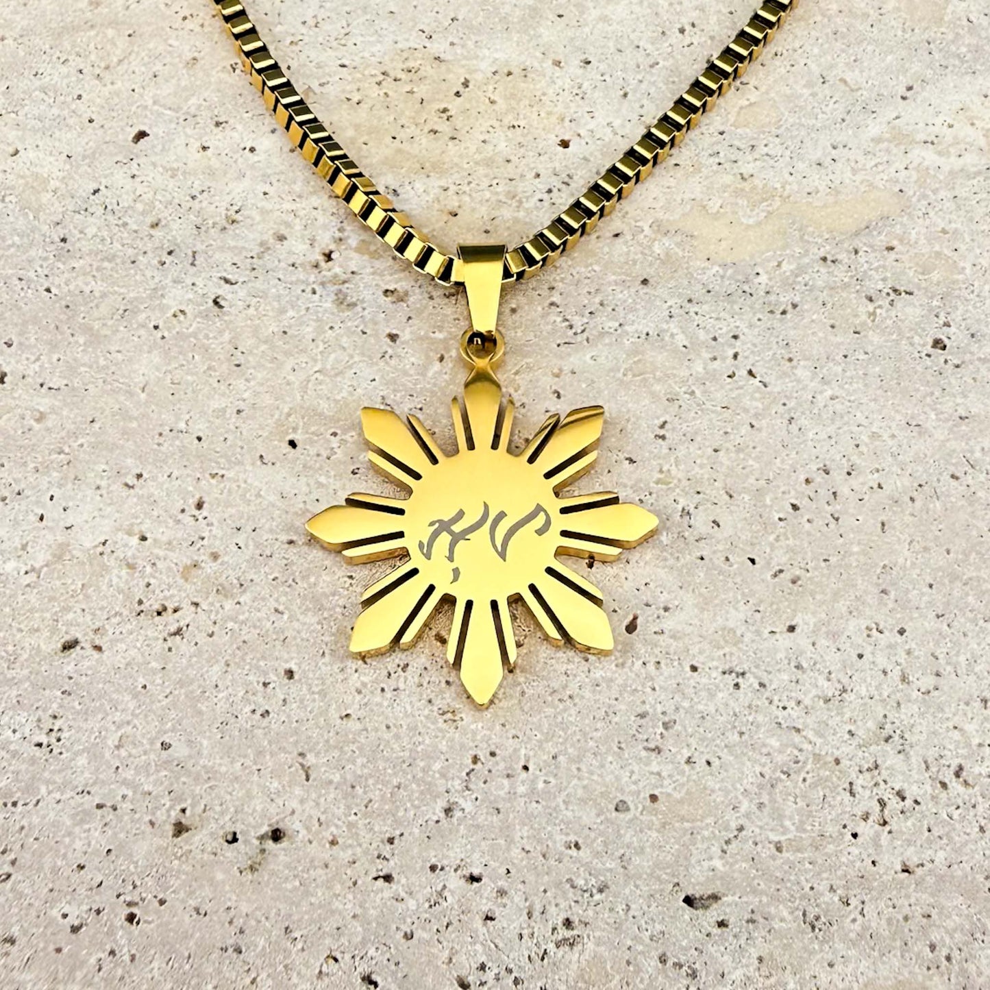 Close-up of a gold Aking Sinta Araw necklace on white marble, featuring a unique bespoke Baybayin script engraving, highlighting the custom personalization service.