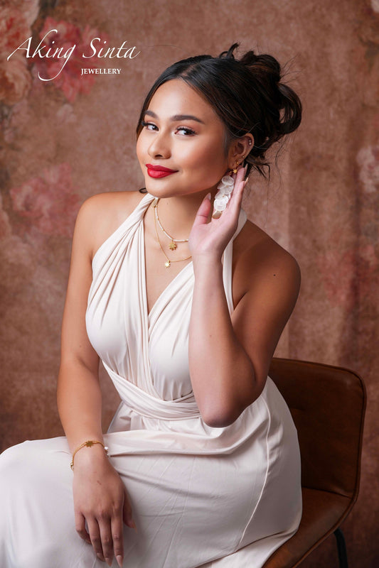Aking Sinta Dainty Araw Necklace in gold worn by model sitting on brown chair, full-body shot, Philippine-inspired jewellery with subtle heritage