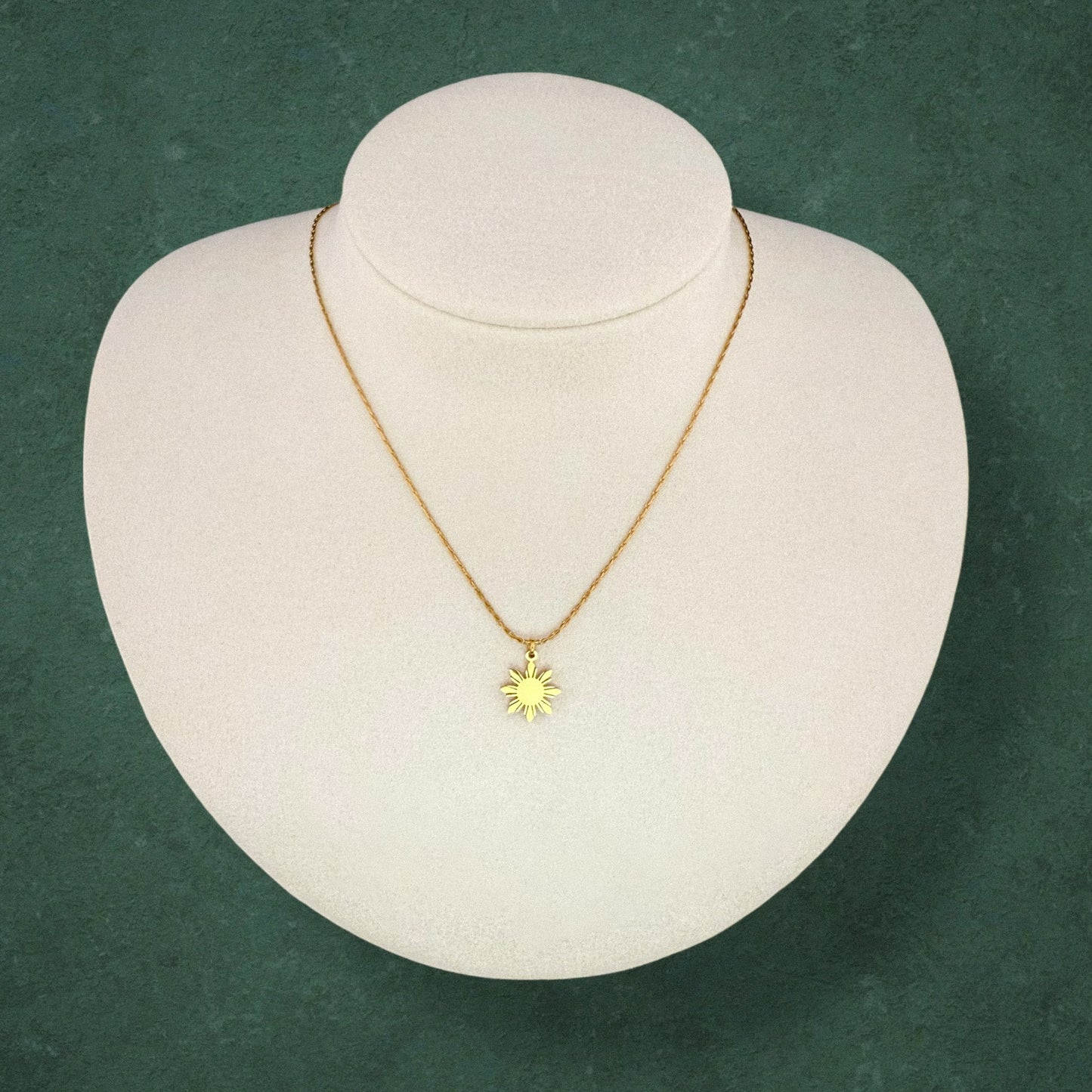 Aking Sinta Dainty Araw Necklace in gold displayed on necklace holder on dark green background, showcasing 8-ray sun design, Philippine-inspired jewellery with subtle heritage