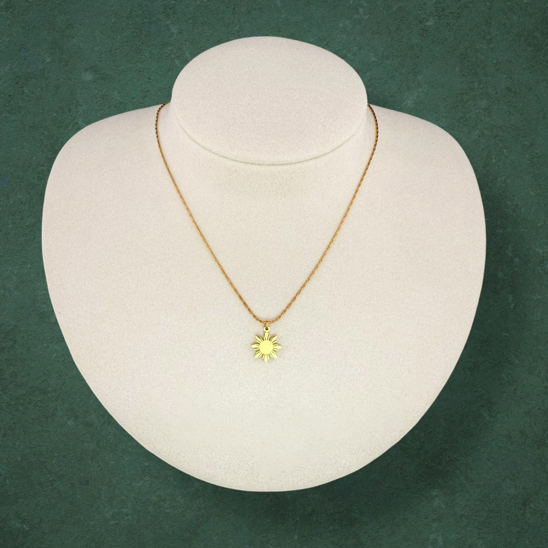 Aking Sinta Dainty Araw Necklace in gold displayed on necklace holder on dark green background, showcasing 8-ray sun design, Philippine-inspired jewellery with subtle heritage
