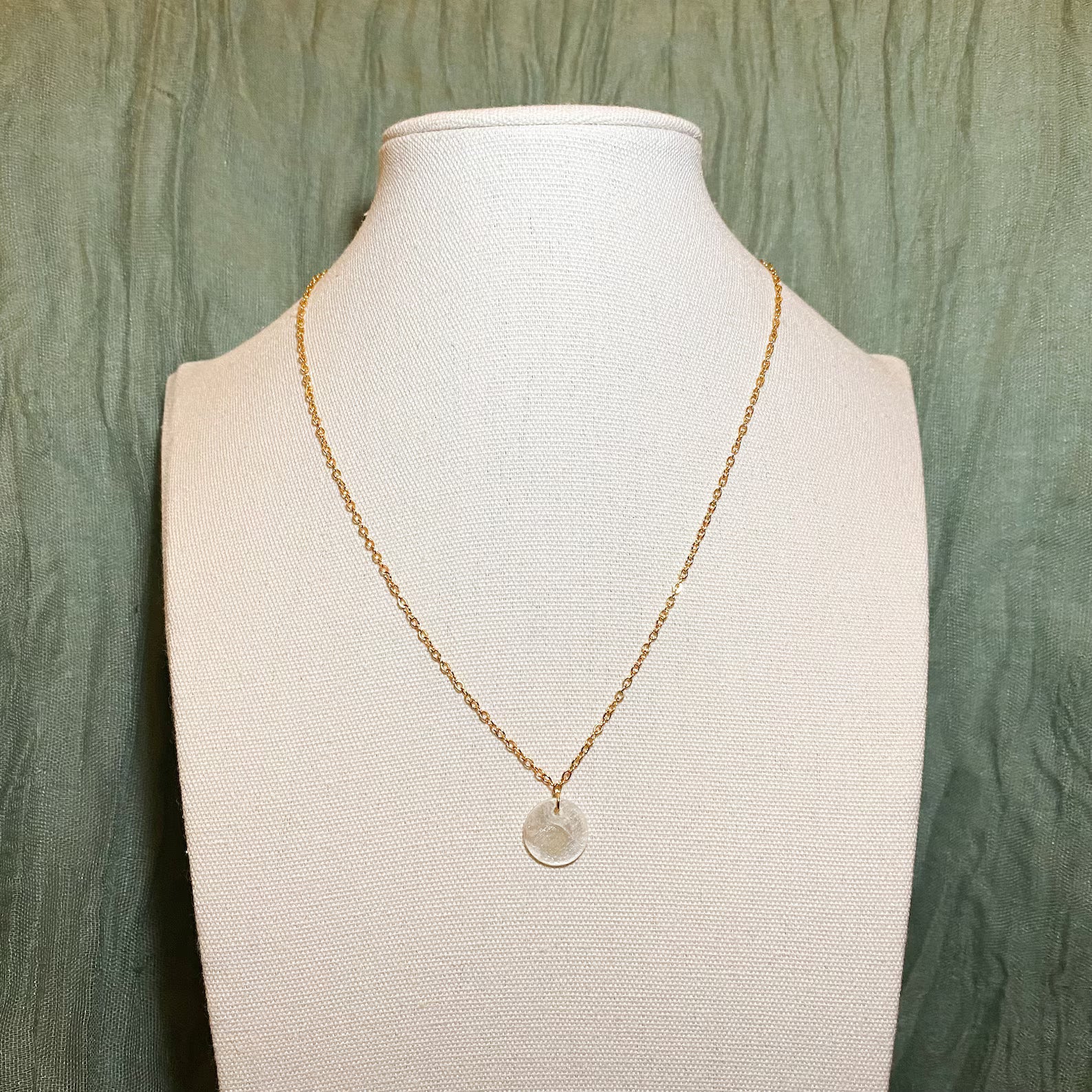 A dainty Aking Sinta necklace with a single circular Capiz shell pendant suspended from a fine gold chain; displayed on a professional white necklace holder to showcase the warm luster and natural iridescence of the shell.