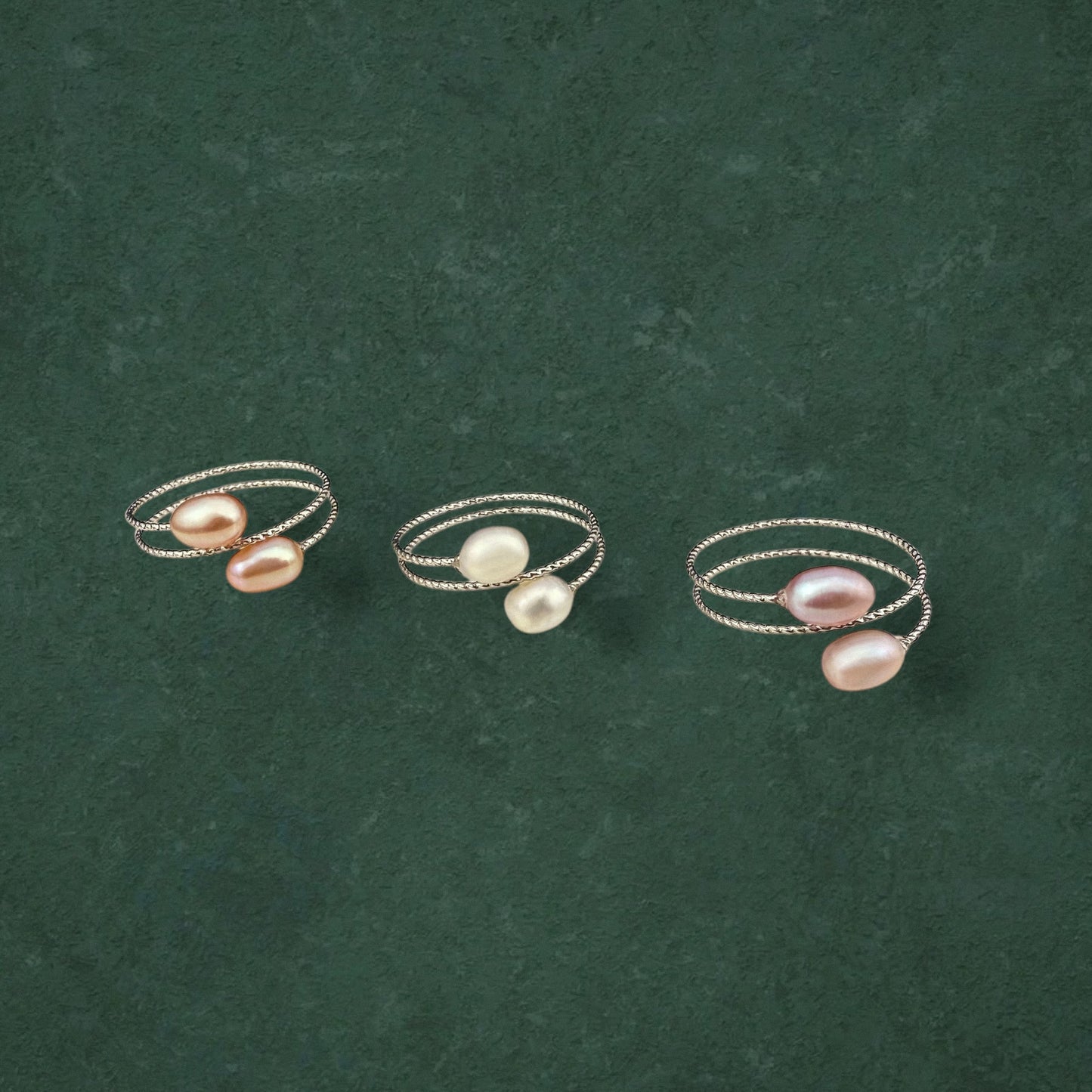 Three Aking Sinta double pearl adjustable rings in Peach, White, and Lilac variants, displayed together on a dark green background.