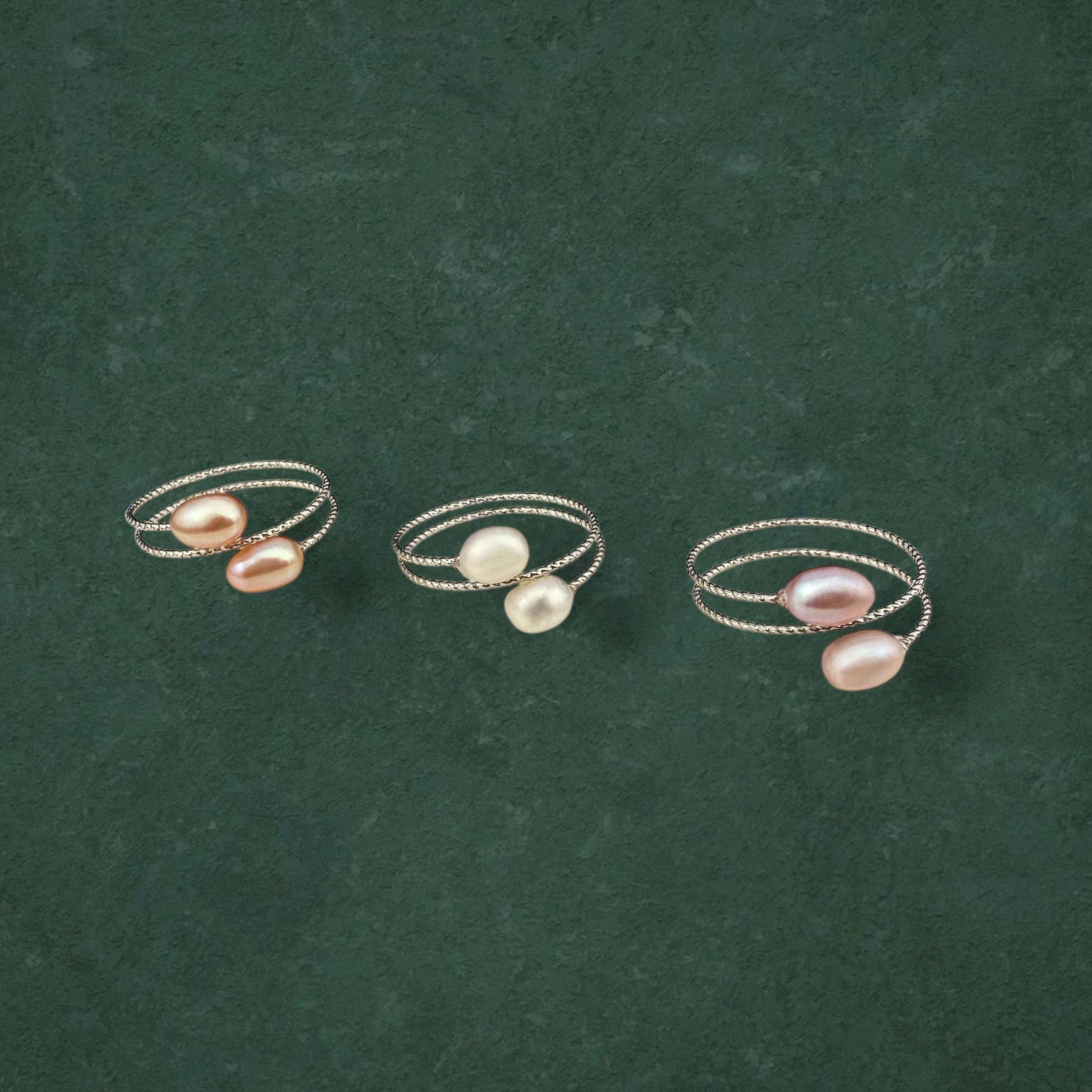 Three Aking Sinta double pearl adjustable rings in Peach, White, and Lilac variants, displayed together on a dark green background.