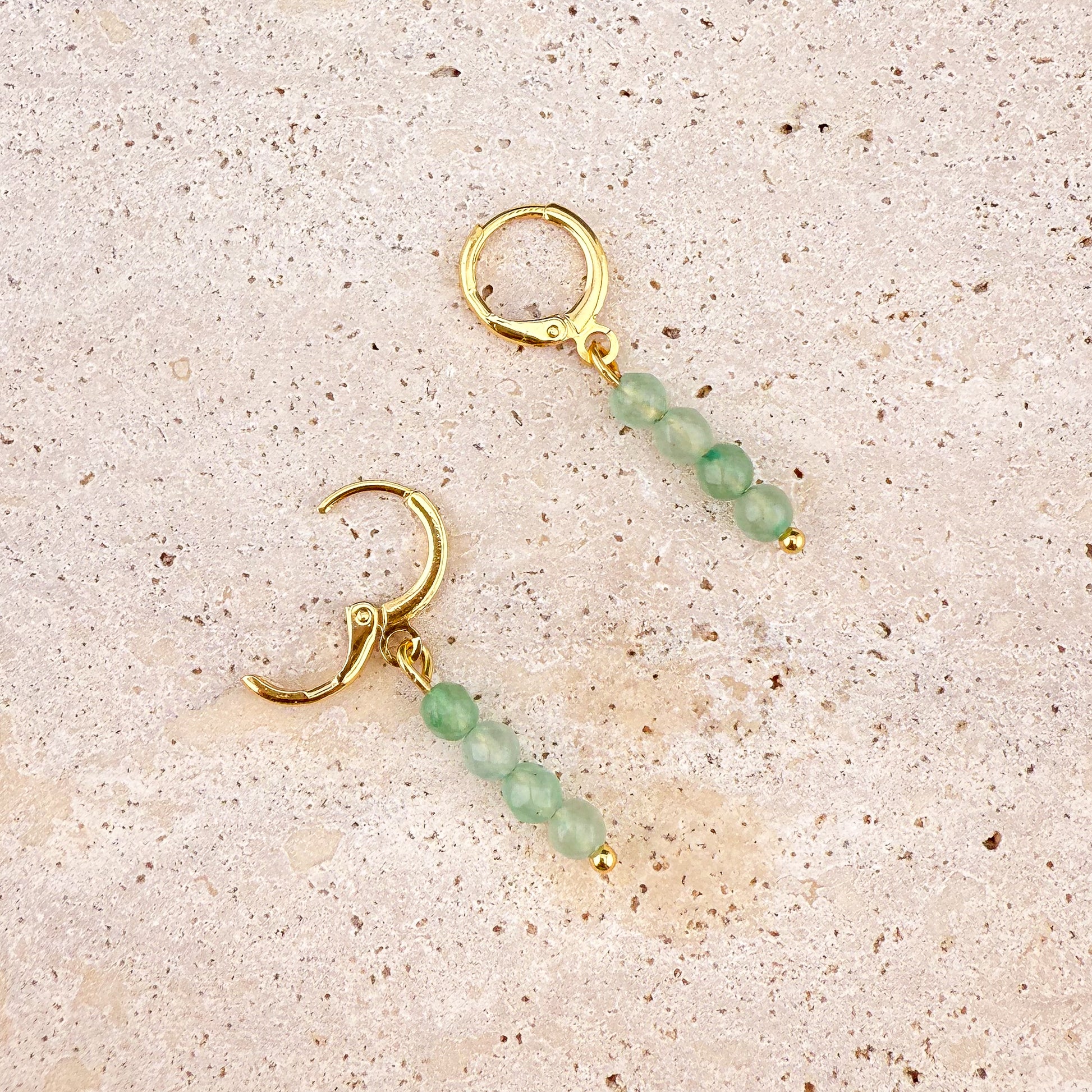 A close-up on white marble of a faceted Green Aventurine huggie earring with its gold hinge clasp open, revealing the secure snapping mechanism and the intricate light-reflecting faces of the deep green gemstone charm.