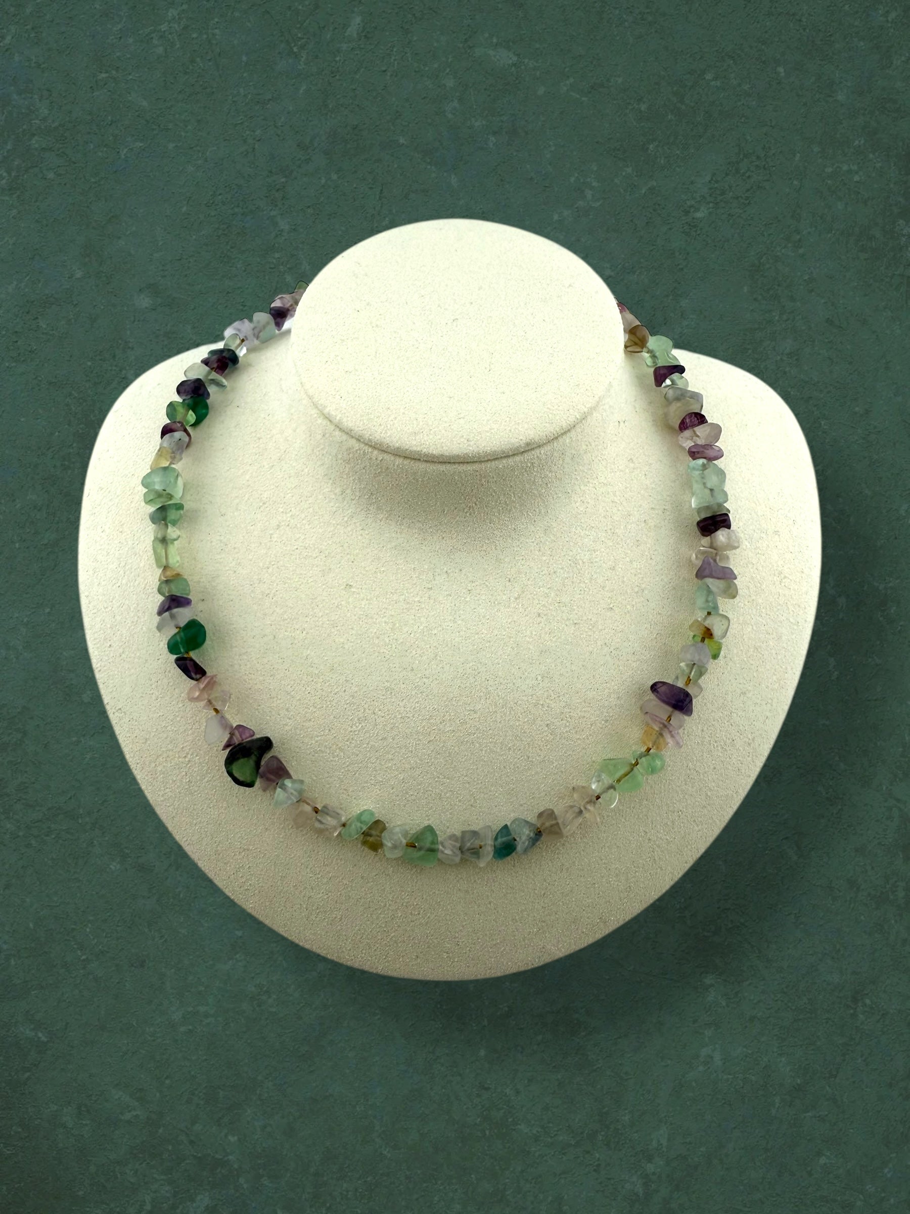 A chunky Aking Sinta necklace made of raw, polished Fluorite nugget beads displayed on a white neck bust; the stones show a natural gradient of translucent purple, green, and clear tones.
