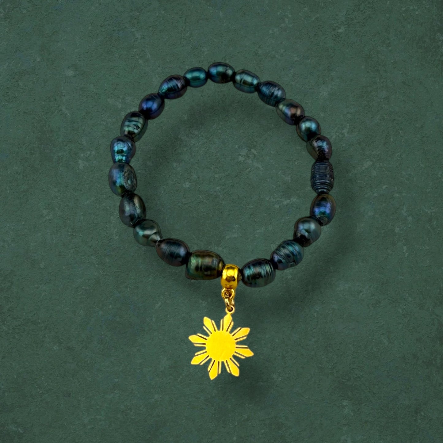 Aking Sinta Freshwater Pearl Stretch Bracelet with dark blue beads and gold Araw charm displayed on dark green background, highlighting natural stone beads and sun motif