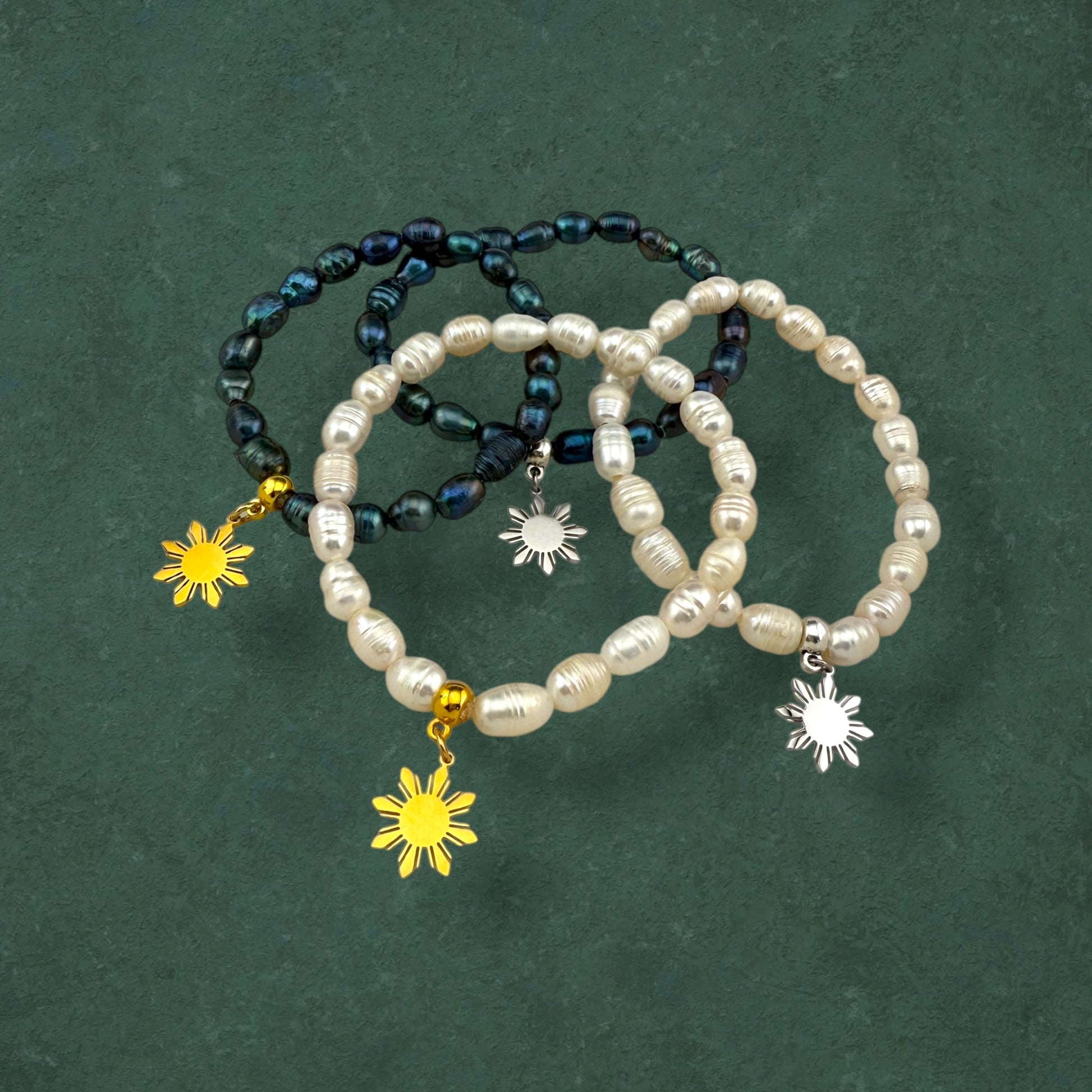 Aking Sinta Freshwater Pearl Stretch Bracelets in all variants – white and dark blue beads, plain, gold and silver Araw charms – displayed on dark green background, highlighting natural stone beads and sun motif