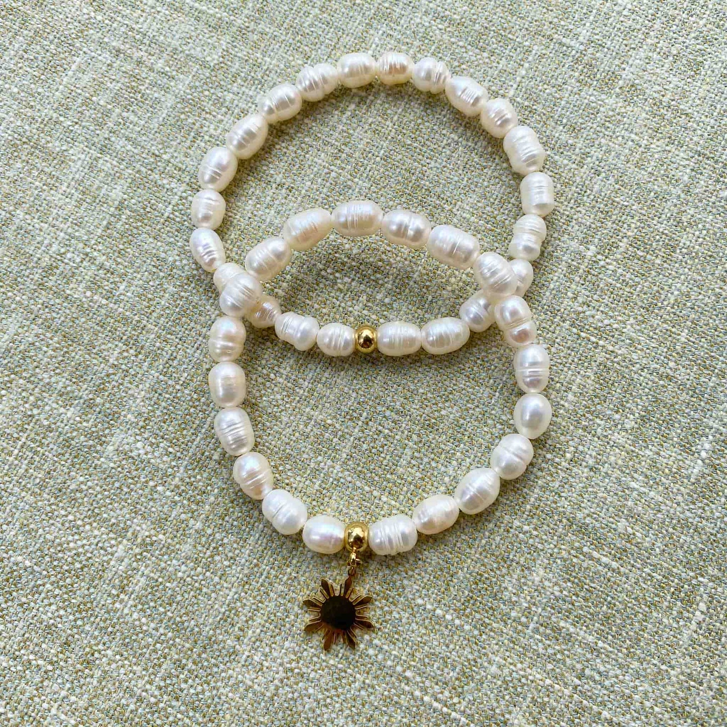 Aking Sinta Freshwater Pearl Stretch Bracelets, plain and with gold Araw charm, displayed on gray woven textured background, highlighting natural white stone beads and sun motif