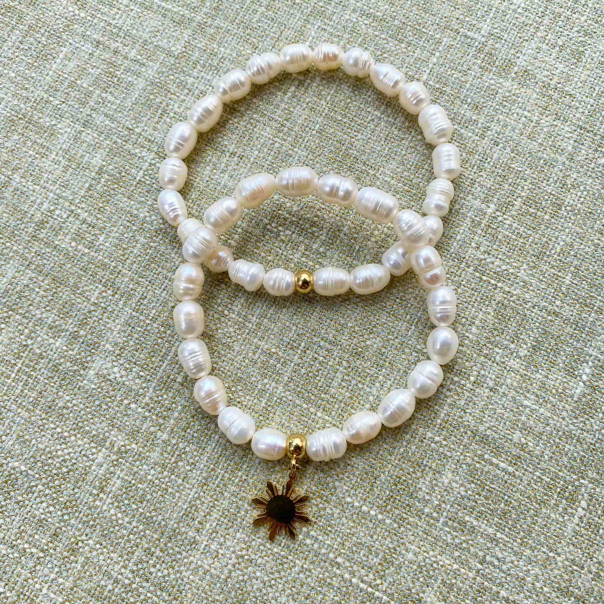 Aking Sinta Freshwater Pearl Stretch Bracelets, plain and with gold Araw charm, displayed on gray woven textured background, highlighting natural white stone beads and sun motif
