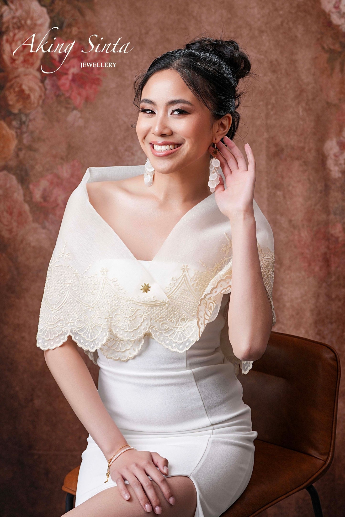 A gold Aking Sinta Araw 8-ray lapel pin used as a decorative lock for a pañuelo scarf on a traditional Filipina dress; worn by a model to secure the handkerchief cloth over the cleavage in a classic Maria Clara style