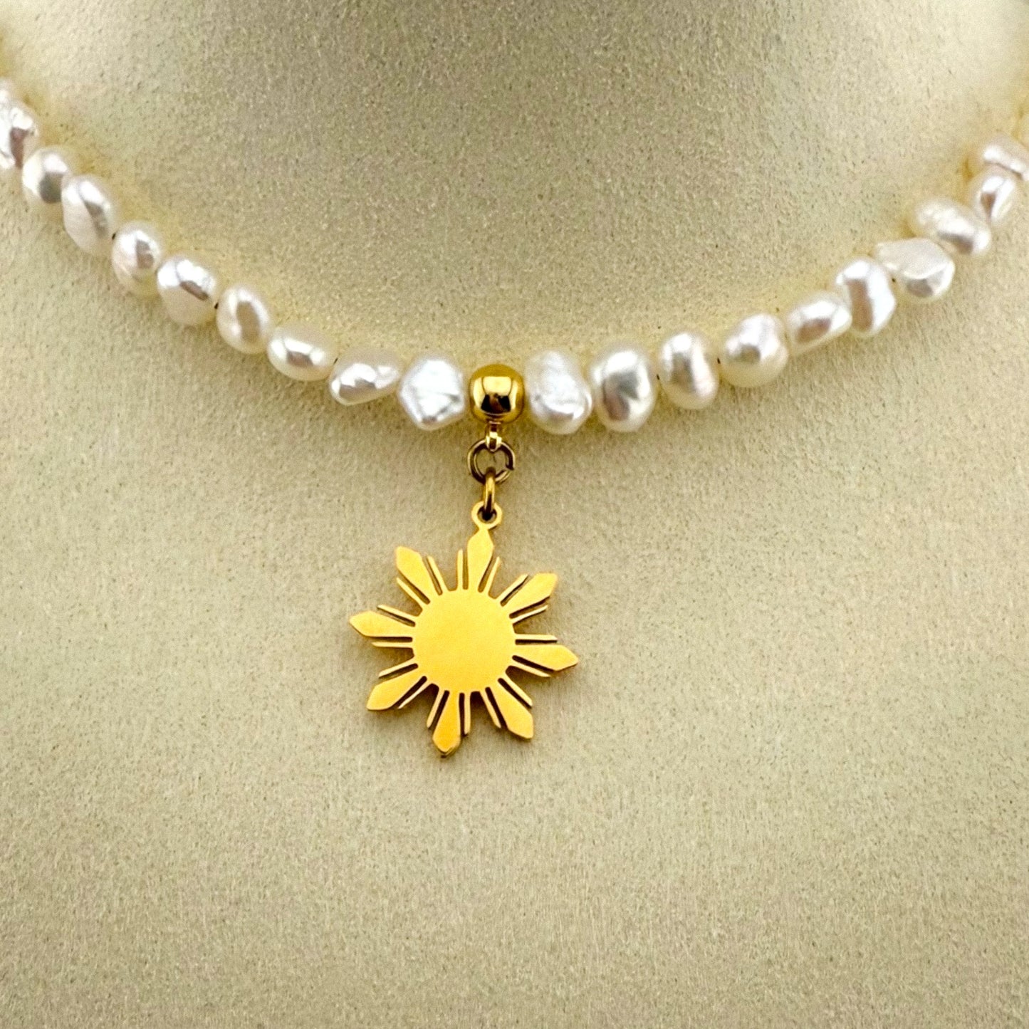 Extreme macro close-up of the Aking Sinta gold 'Araw' sun charm on a pearl necklace, showing the detailed rays and polished gold finish.