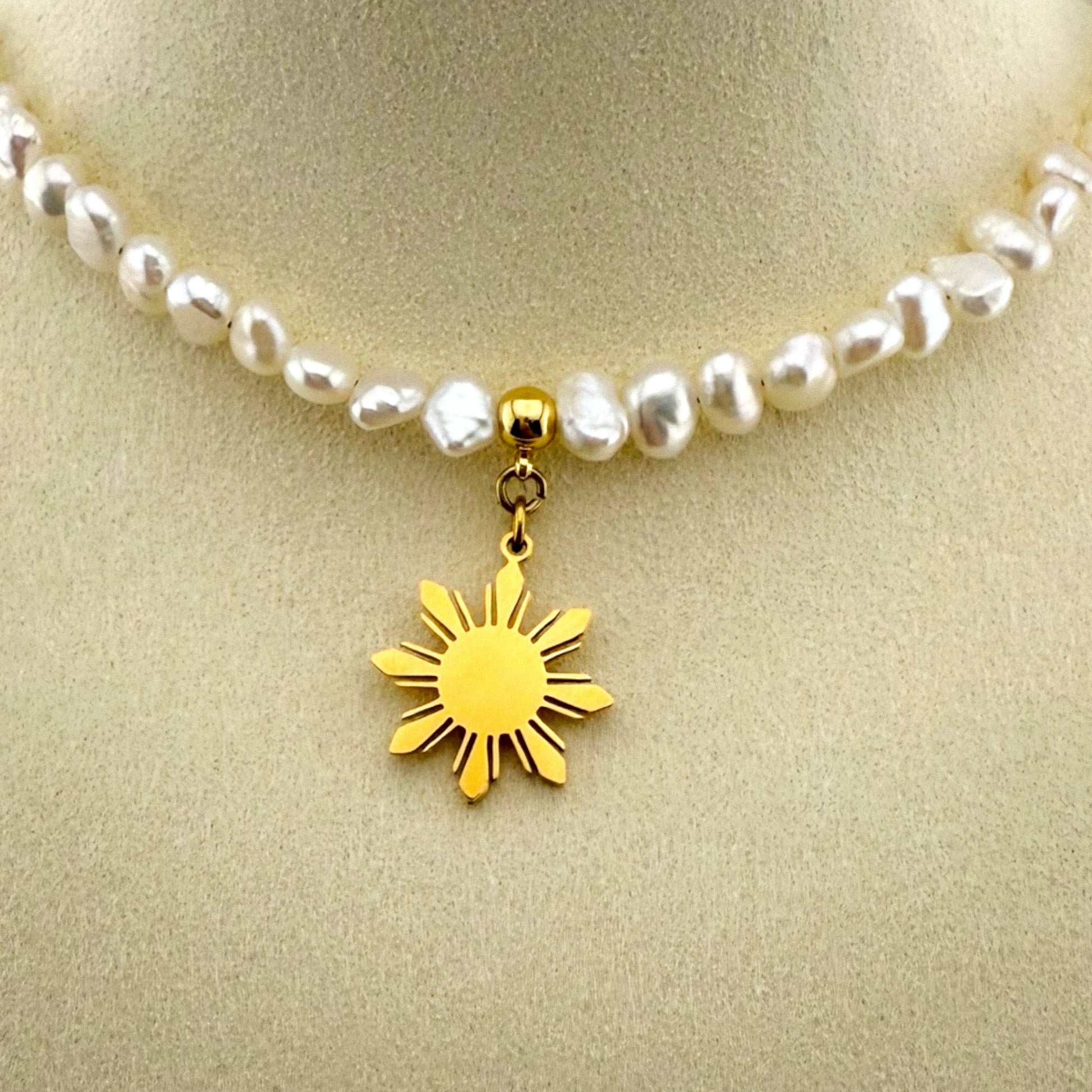 Extreme macro close-up of the Aking Sinta gold 'Araw' sun charm on a pearl necklace, showing the detailed rays and polished gold finish.