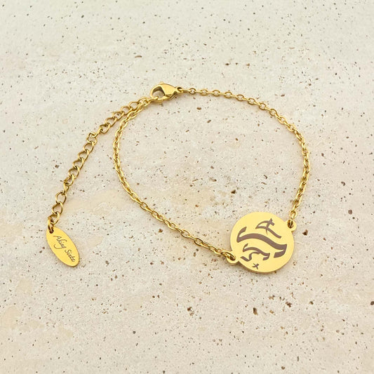 A gold Aking Sinta coin bracelet featuring a bespoke engraving in ancient Filipino Baybayin script. The bracelet includes a lobster clasp and an adjustable extender chain with a signature "Aking Sinta" oval tag, displayed on a light natural stone surface.
