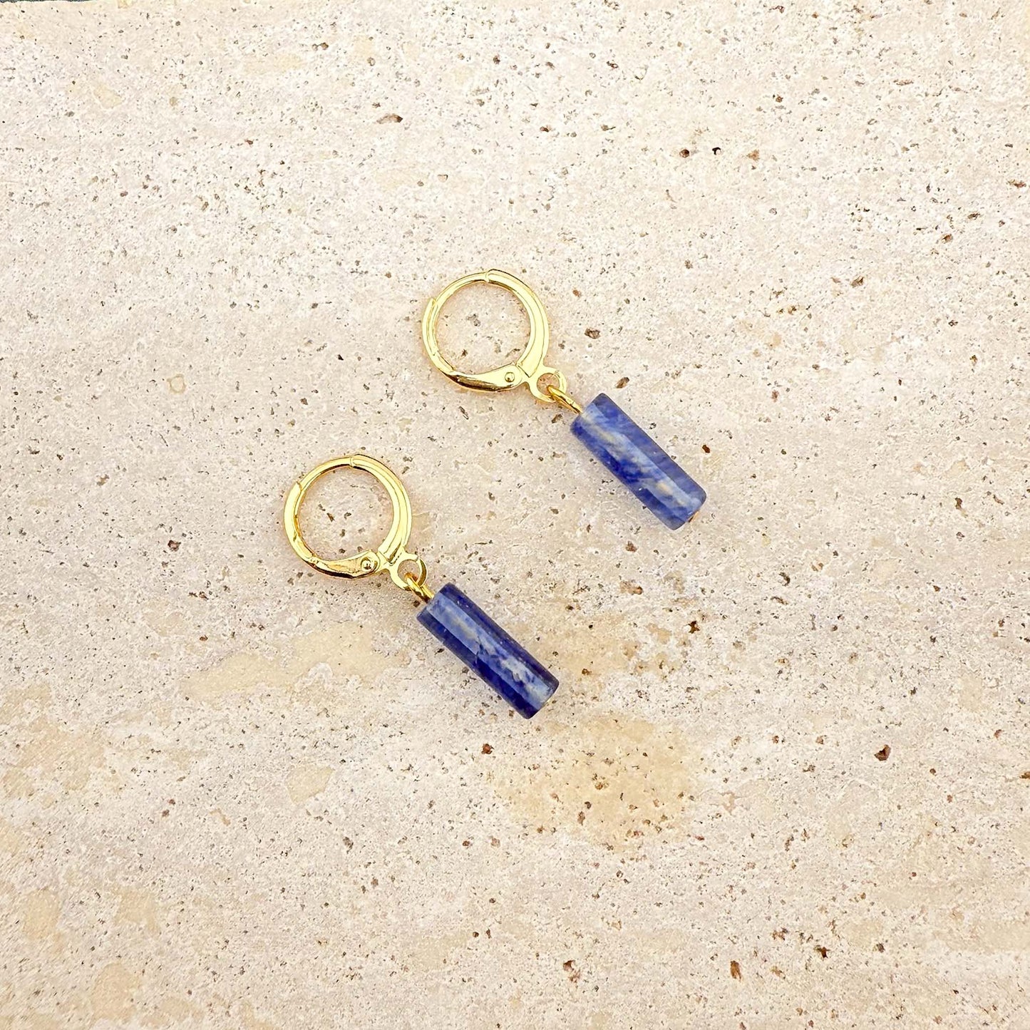 Gold Aking Sinta huggie earrings with rectangular blue watermelon column-cut glass charms on a white marble surface.

