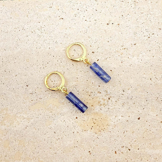 Gold Aking Sinta huggie earrings with rectangular blue watermelon column-cut glass charms on a white marble surface.

