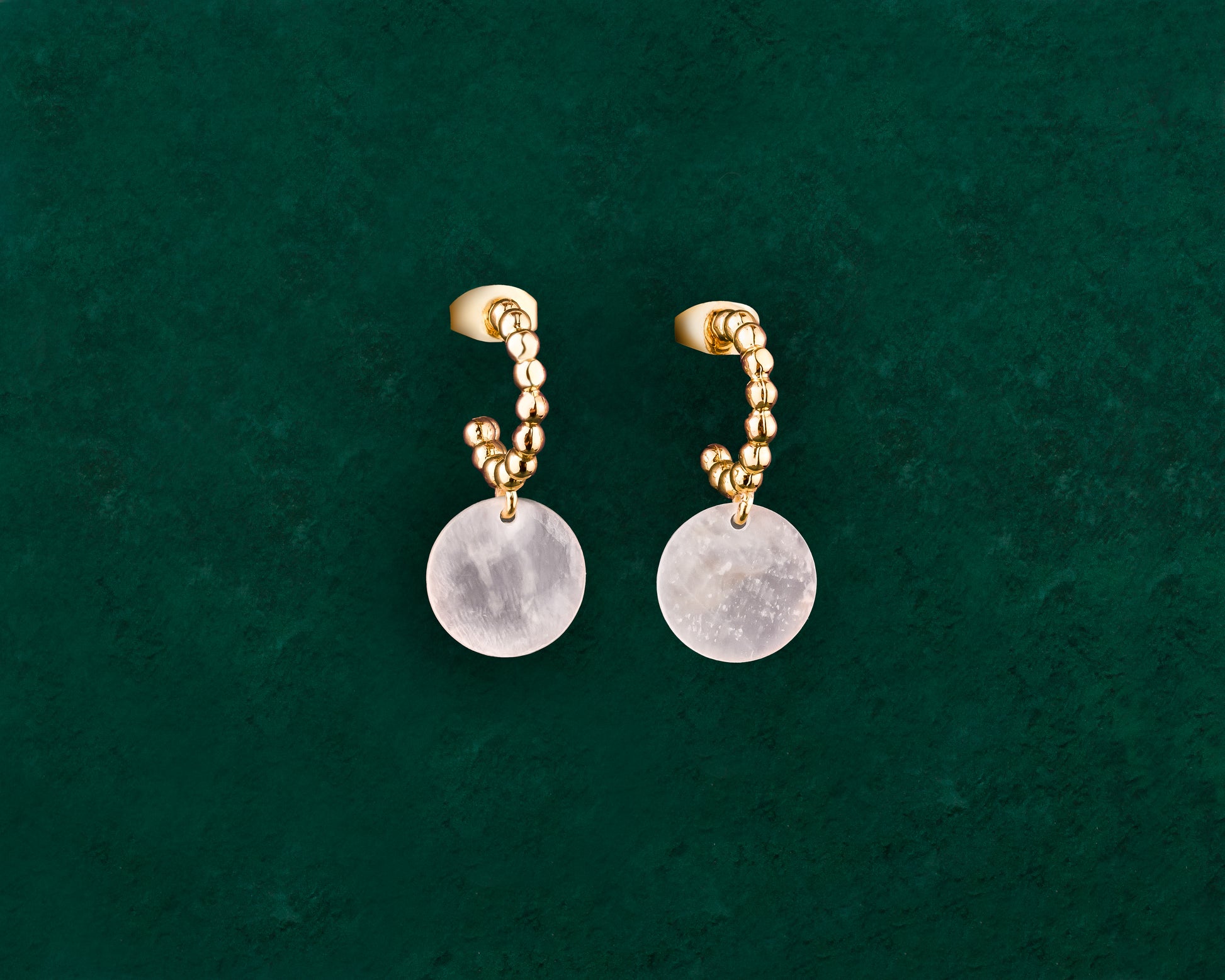 A pair of Aking Sinta gold Bubble Hoop Stud earrings on a dark green background; the hoops feature a unique "bubble" beaded texture and a single round, iridescent white Capiz shell charm dangling from the base.