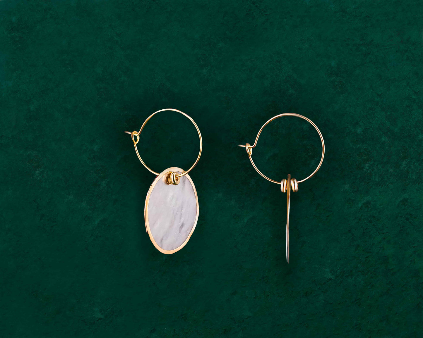 A pair of Aking Sinta Gold Lined Capiz Shell Hoop Earrings on a dark green background; featuring round, flat white Capiz shell disks with a polished gold metal trim around the entire outer edge, hanging from a simple gold ear wire.