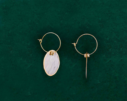A pair of Aking Sinta Gold Lined Capiz Shell Hoop Earrings on a dark green background; featuring round, flat white Capiz shell disks with a polished gold metal trim around the entire outer edge, hanging from a simple gold ear wire.