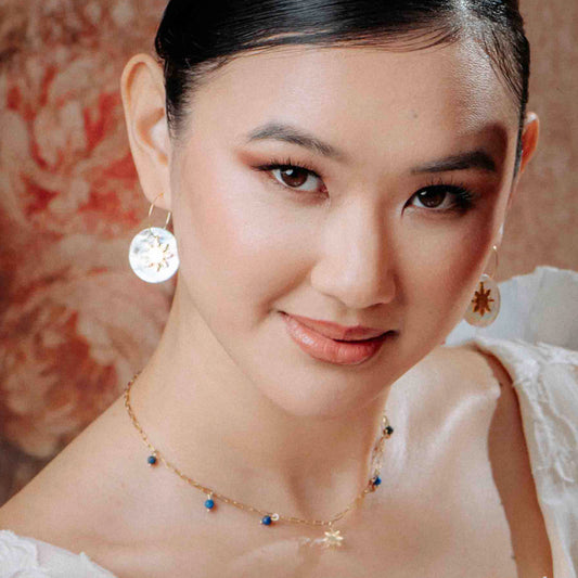 Model wearing an Aking Sinta gold paperclip chain necklace with two small charms: a dainty 8-ray Araw sun and a deep blue Lapis Lazuli gemstone drop.