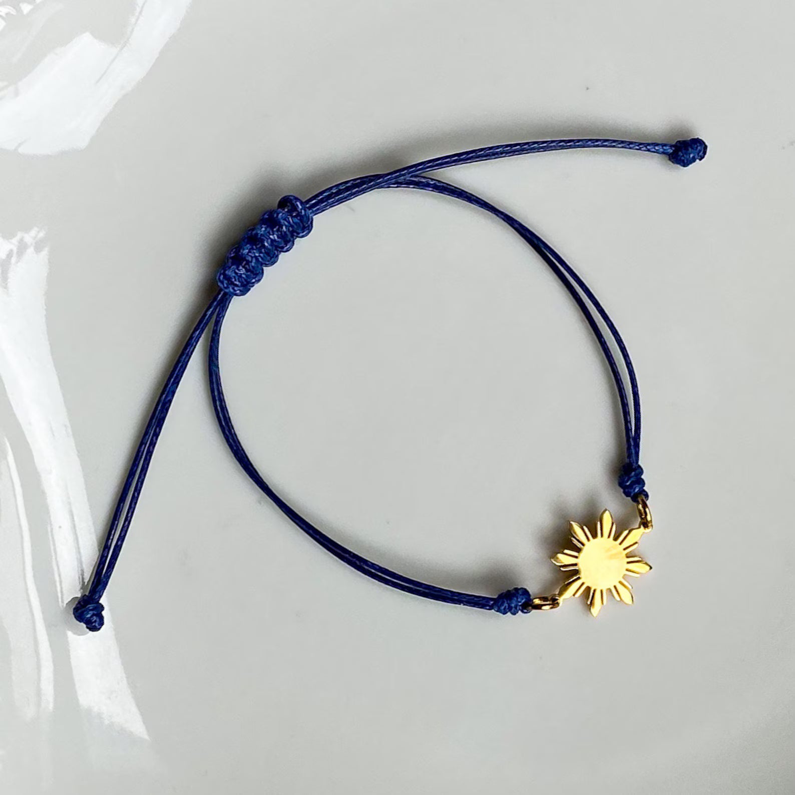 Aking Sinta unisex friendship bracelet featuring a radiant gold 8-ray Philippine sun charm on a vibrant blue cord; photographed on a white background to showcase the vivid color contrast and symbolic design.
