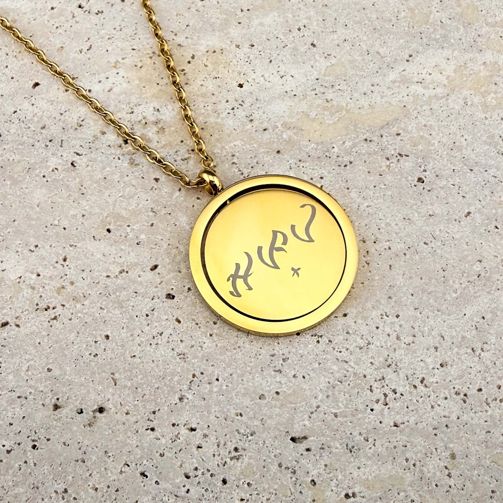 Close-up of the Aking Sinta gold Spinning Coin necklace, featuring bespoke Baybayin script engraving on the rotating charm, resting on a white marble slab.