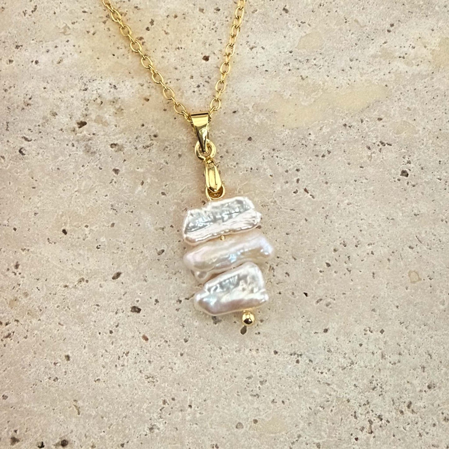 Gold Aking Sinta necklace with three flat, iridescent white Keshi pearls spaced on a delicate chain over white marble.