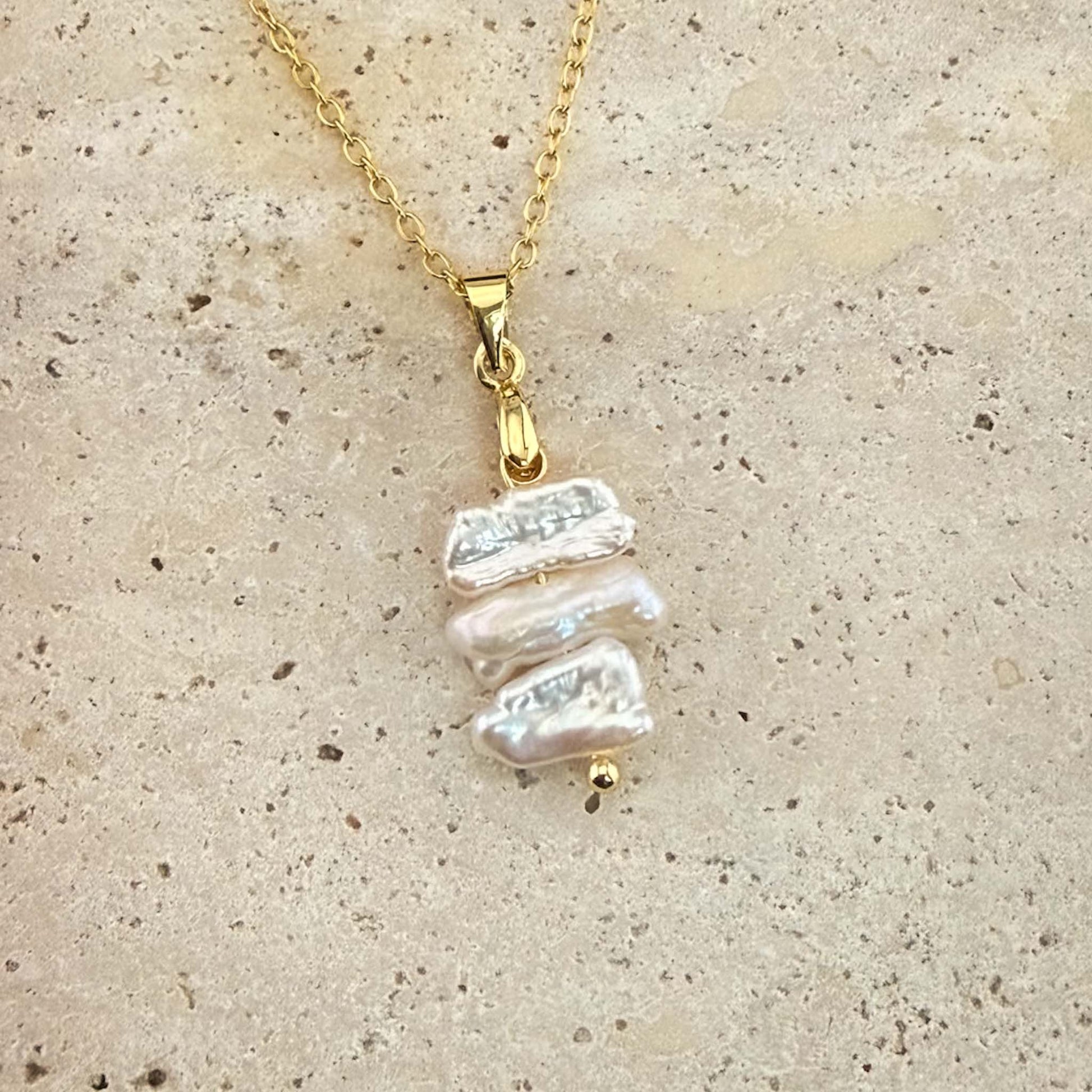 Gold Aking Sinta necklace with three flat, iridescent white Keshi pearls spaced on a delicate chain over white marble.