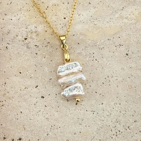 Gold Aking Sinta necklace with three flat, iridescent white Keshi pearls spaced on a delicate chain over white marble.
