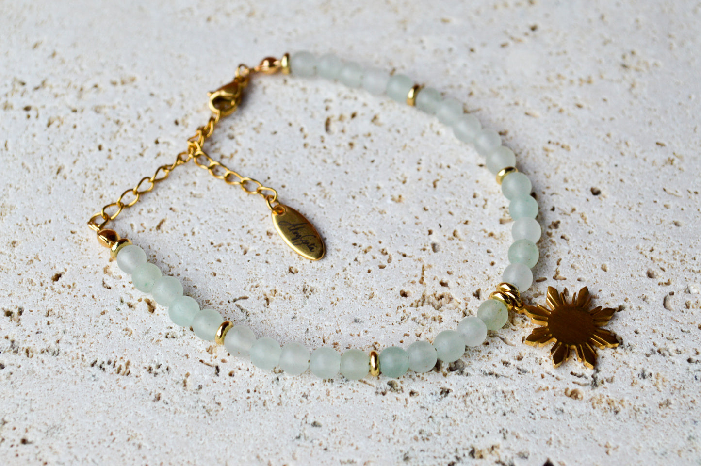 Close-up of Aking Sinta Green Aventurine Bracelet with Araw sun charm displayed on white rock-textured background, highlighting natural green stone beads
