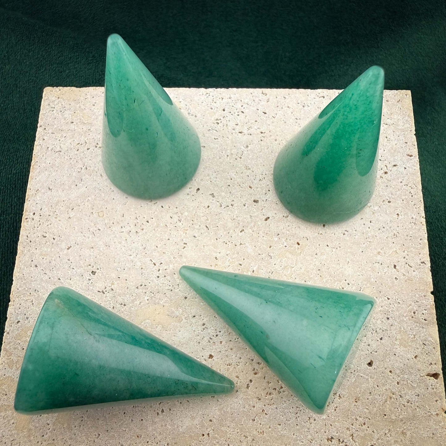Four polished green aventurine gemstone ring cones arranged on a square light stone block. These conical jewelry displays feature natural green marbled patterns and are set against a dark green velvet background.