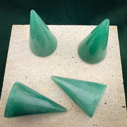 Four polished green aventurine gemstone ring cones arranged on a square light stone block. These conical jewelry displays feature natural green marbled patterns and are set against a dark green velvet background.