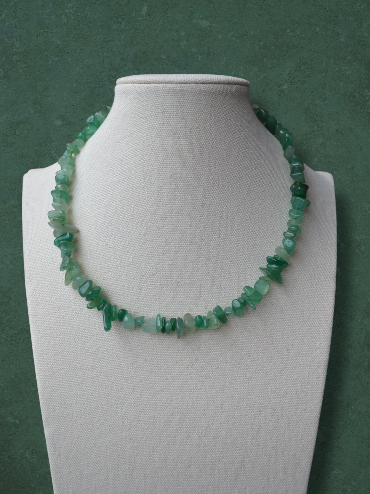 A chunky Aking Sinta necklace of raw, polished Green Aventurine nugget beads strung closely together without spacers; the strand is displayed on a white professional neck bust against a solid forest-green backdrop.