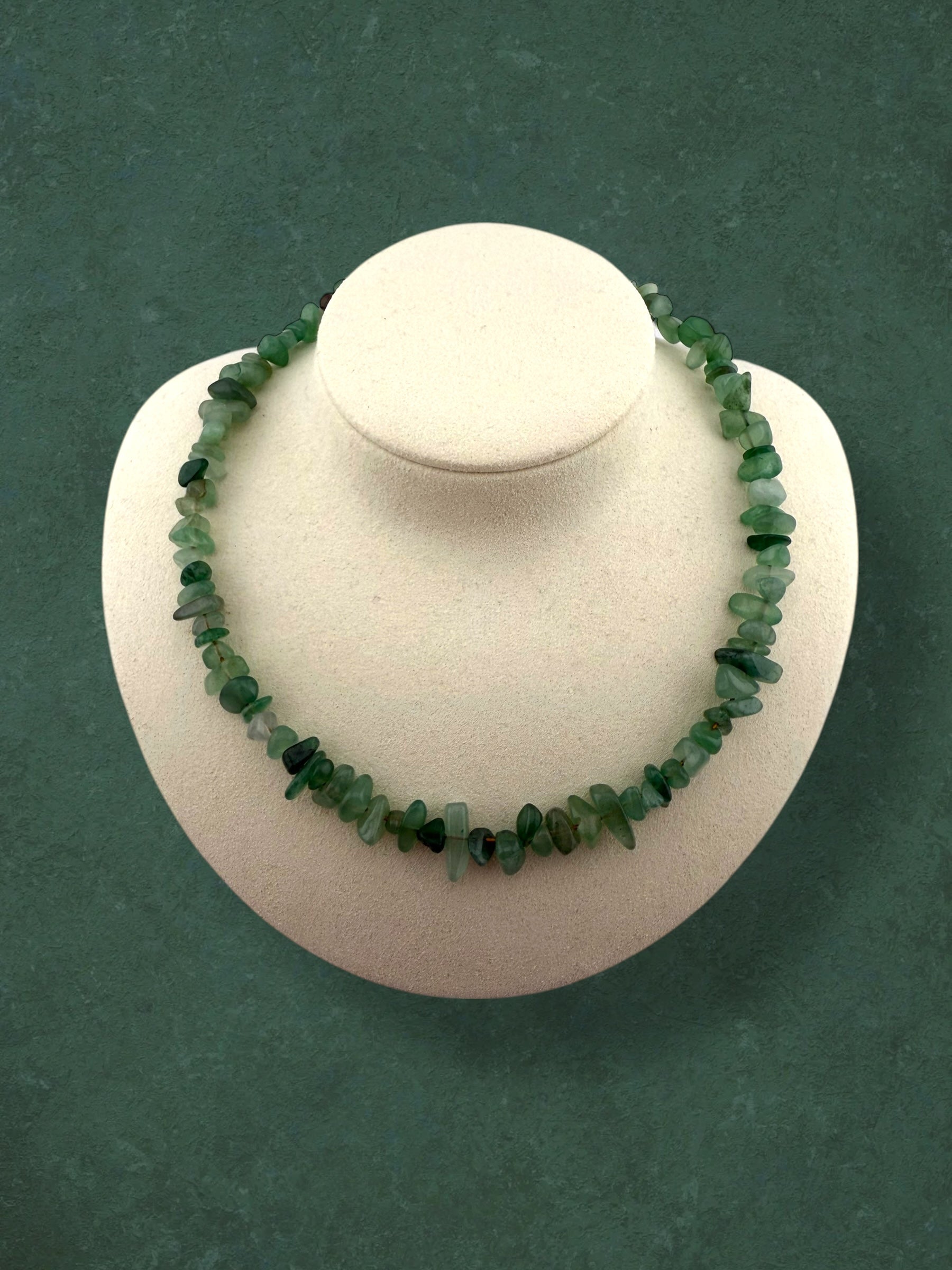 A statement-style Aking Sinta necklace made of large, polished Green Aventurine nuggets without spacers; the strand is displayed on a white neck bust against a solid deep green background to show how it drapes around the neck.