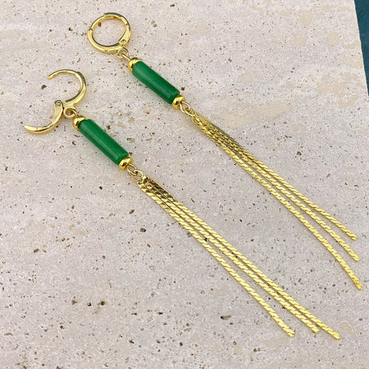 Macro view of a Green Jade column tassel earring on gray marble with the gold huggie clasp open, showing the internal hinge and the detailed attachment of the jade stone and gold chain fringe.