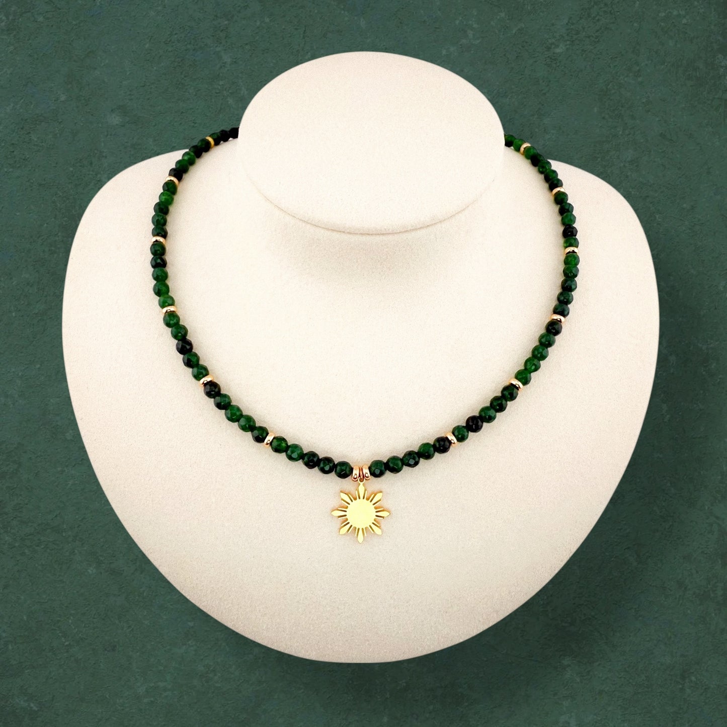 Aking Sinta Green Jade beaded necklace on a white display bust; featuring vibrant, polished green gemstones accented with small gold beads throughout the strand and a central gold 8-ray Araw sun charm