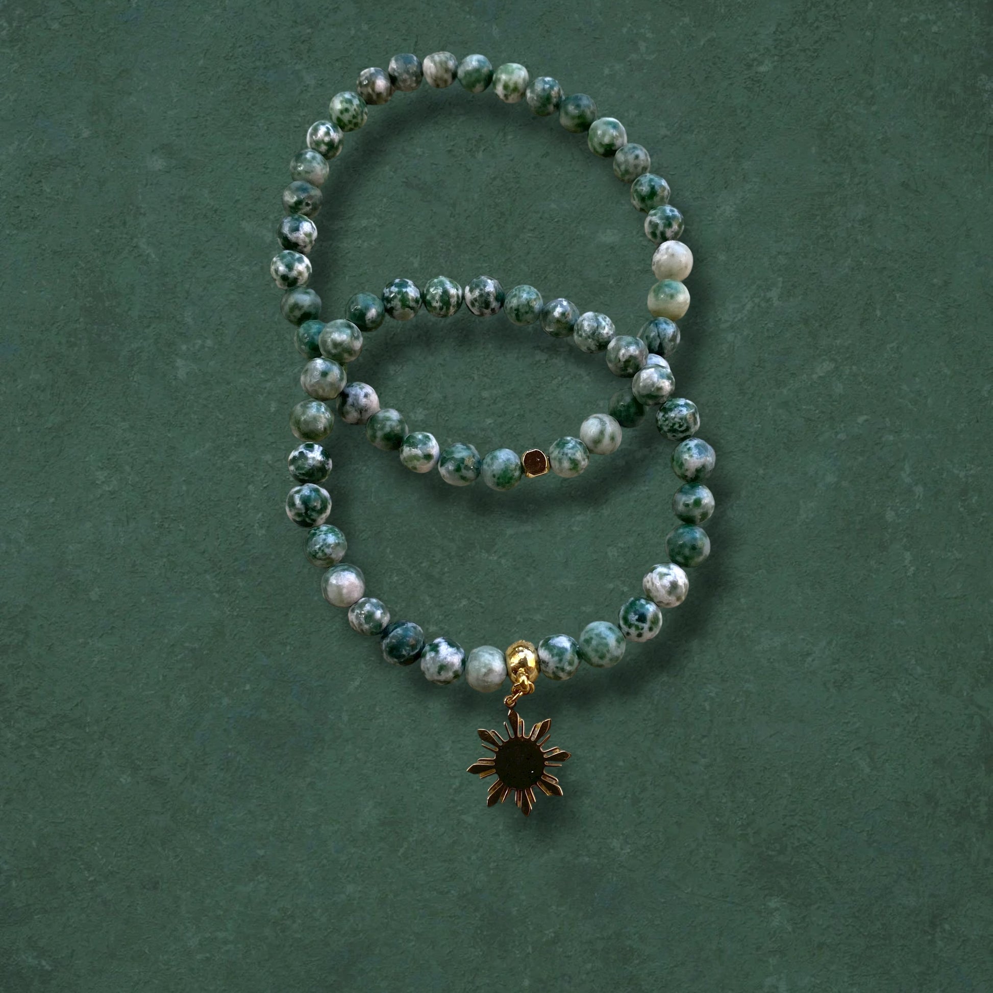 Close-up of Aking Sinta Green Spot Jasper Stretch Bracelet, plain and with Araw sun charm, on green background, highlighting natural stone beads and Philippine-inspired design