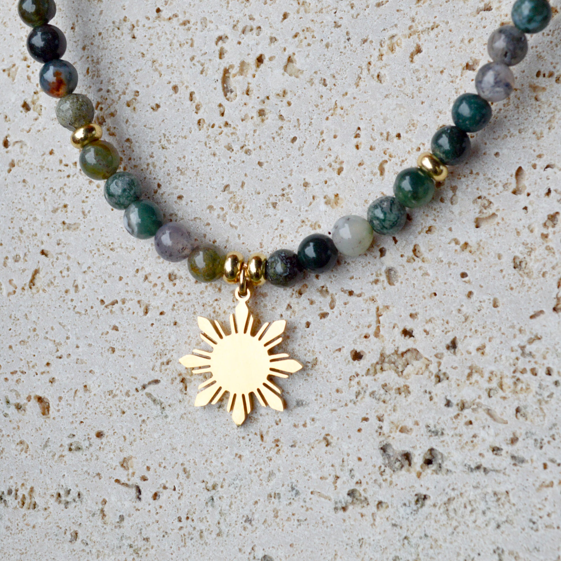 Close-up of Aking Sinta Indian Agate Necklace gold variant with Araw sun charm on rock-like textured background, highlighting natural stone beads and Philippine-inspired design