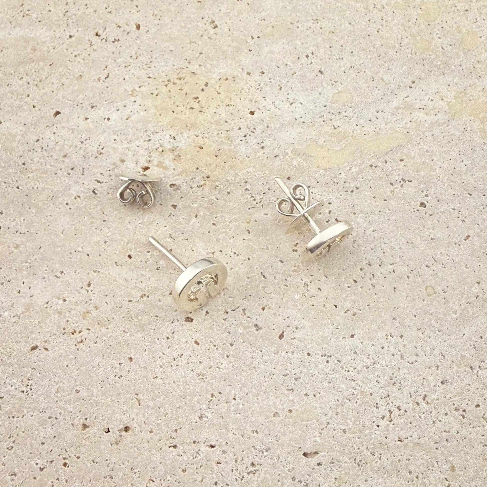 A close-up view of Aking Sinta sterling silver Lingling-O stud earrings. The image shows the butterfly scroll backs and post detail of the circular Filipino-inspired studs, displayed on a light natural stone surface