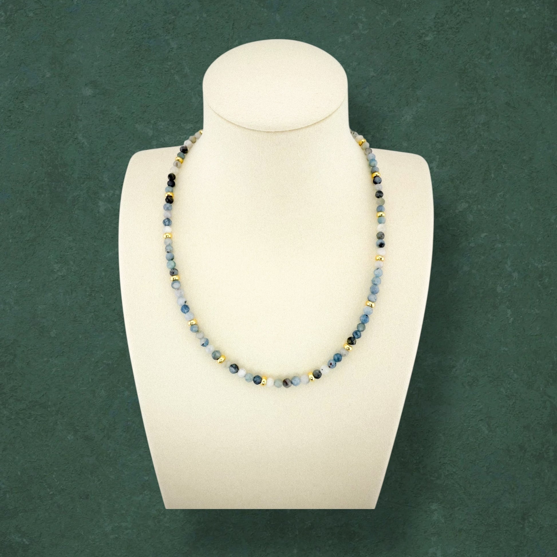 Full-length Aking Sinta Dirty Aquamarine necklace without a charm, draped over a white elongated torso bust; the long strand features light and dark blue beads with small gold accents reaching the hip level.