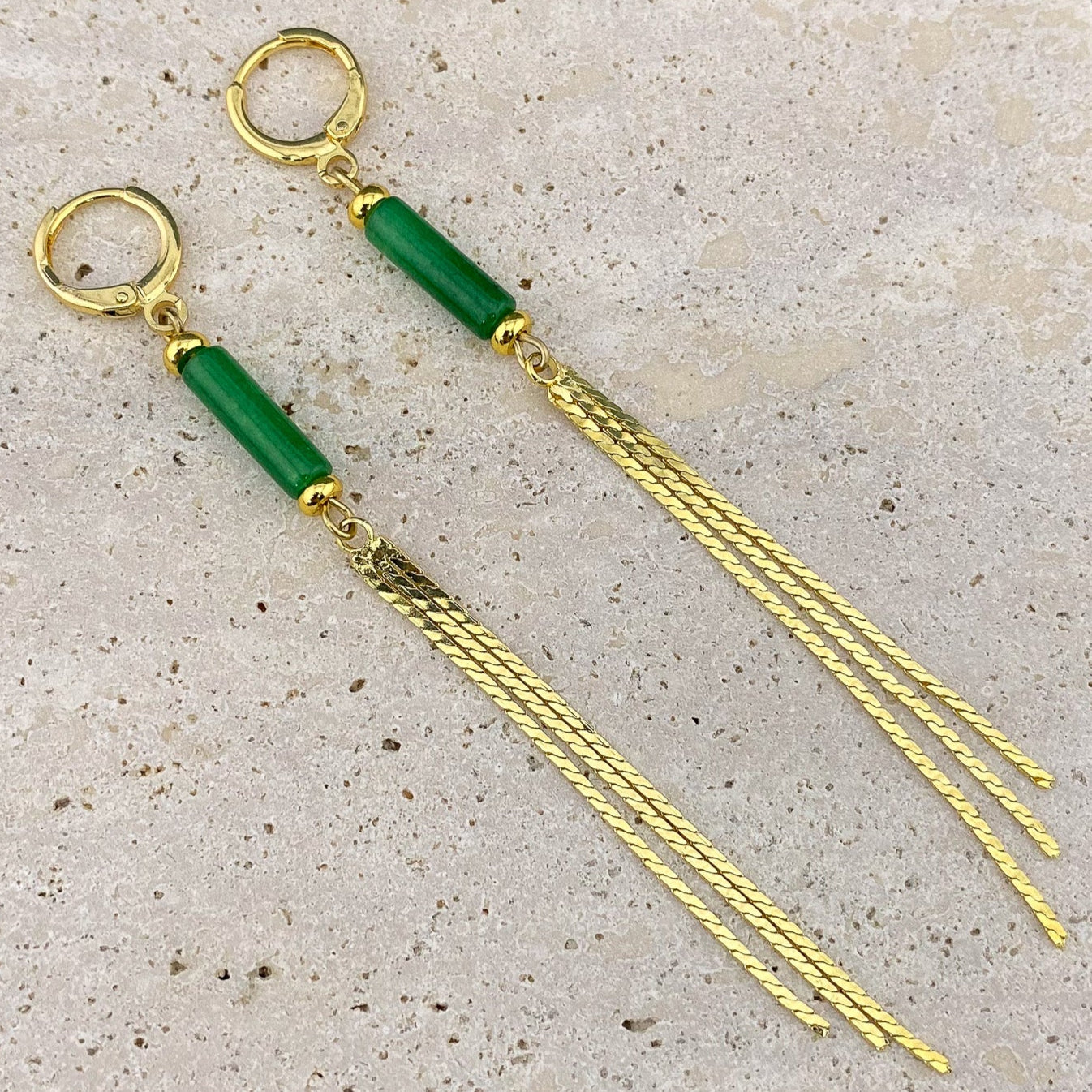 An extreme macro close-up of a Green Jade column earring on gray marble, showing the translucent dark green texture of the stone and the intricate individual links of the gold chain tassels.